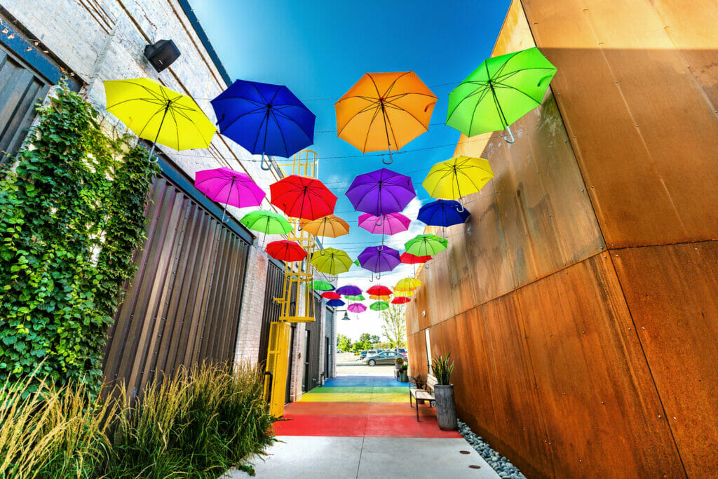 Different colored umbrellas hanging from wires above an alleyway at Easton. The sidewalk in the alleyway is painted with rainbow colors.