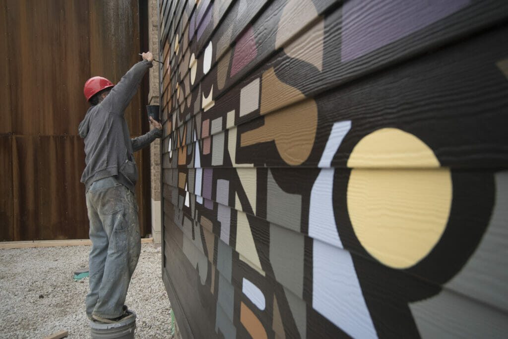 Artist painting a mural onto the side of Crimson, a coffee shop at Easton.