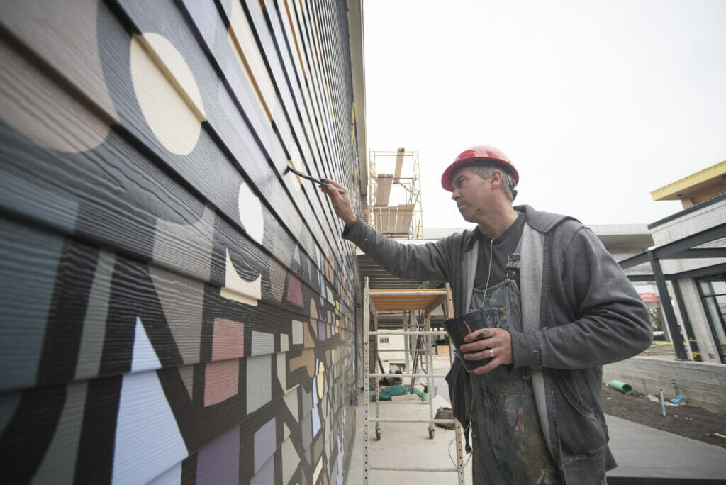 Artist painting a mural onto the side of Crimson, a coffee shop at Easton.