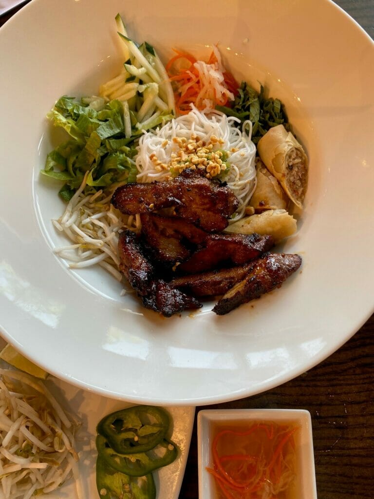 A chicken and rice noodles dish with vegetables and egg rolls in a bowl.