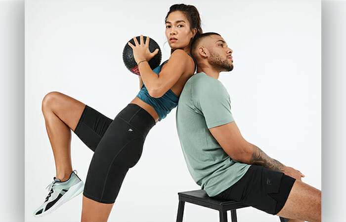 A girl holding a basketball wearing Fabletics athleticwear and leaning against a guy in a chair who is also wearing Fabletics athletic gear.