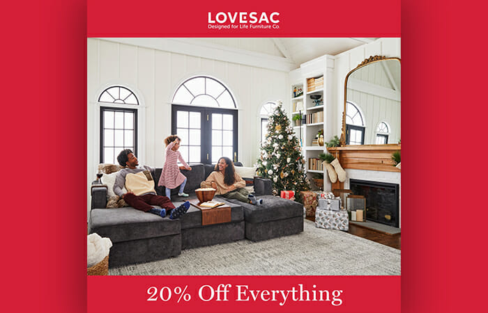 A family sitting on a Lovesac couch in their living room with holiday decorations everywhere and promotional copy that reads Lovesac 20% Off Everything.