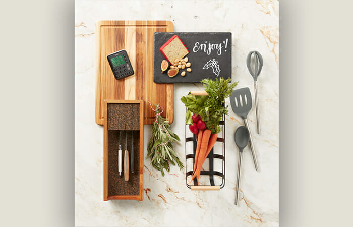 Kitchen items laid out on a counter. Includes spatulas, spoons, a cutting board, and some vegetables. and knives