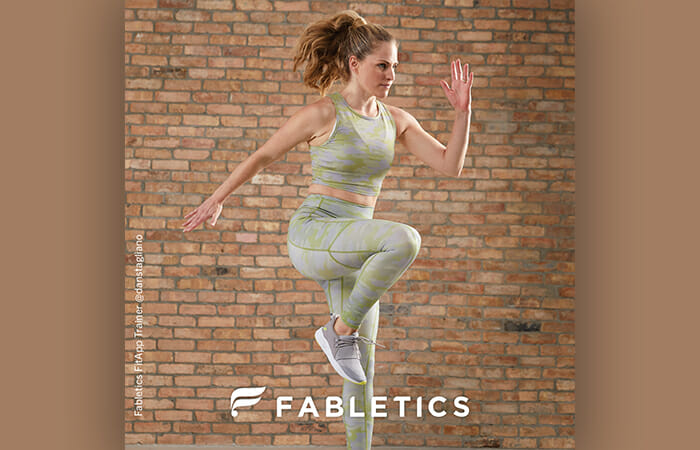A woman wearing Fabletics workout gear and jumping in the air.