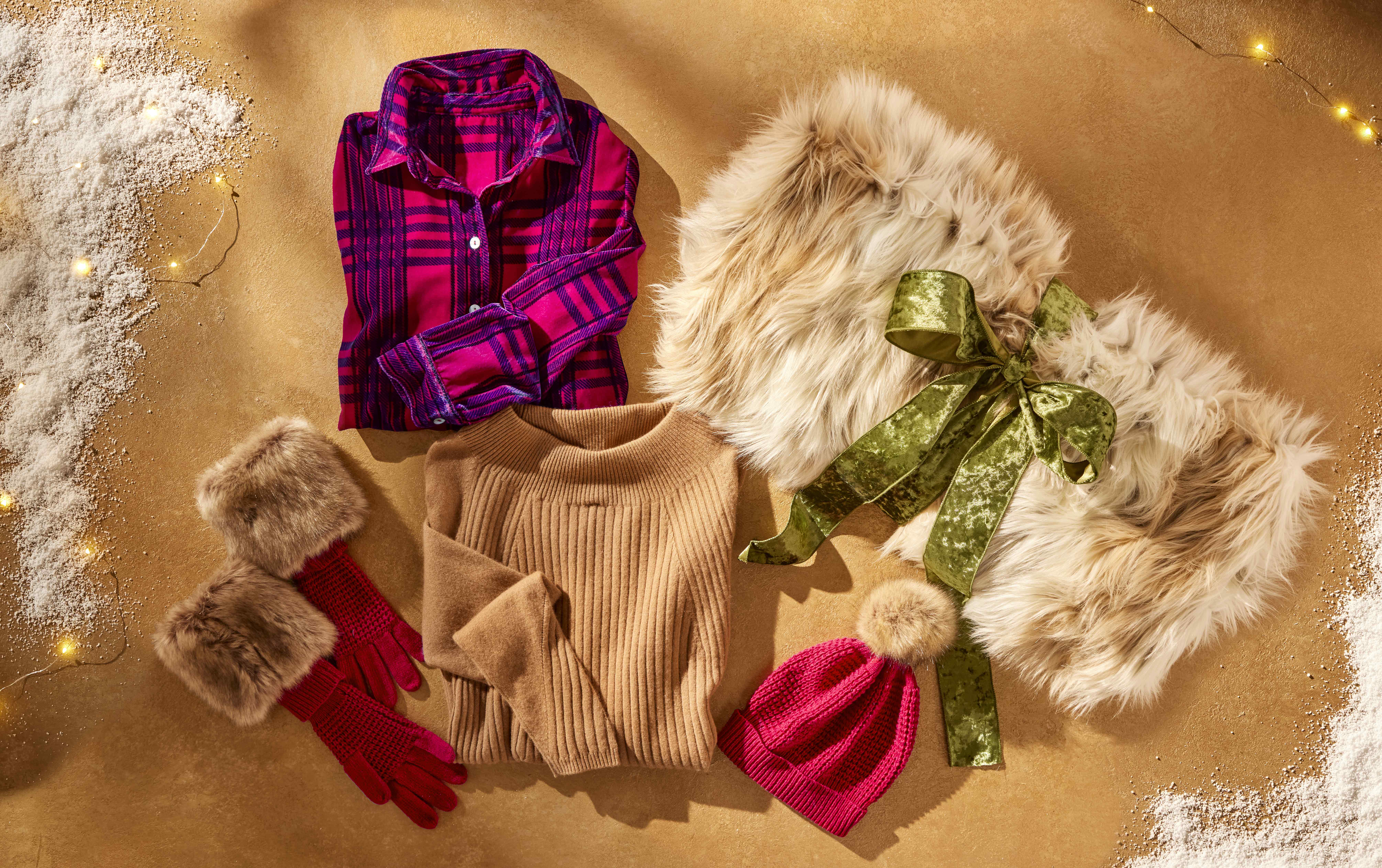 Soft Surroundings sweaters laid out on a table with gloves and a furry blanket wrapped in a bow.
