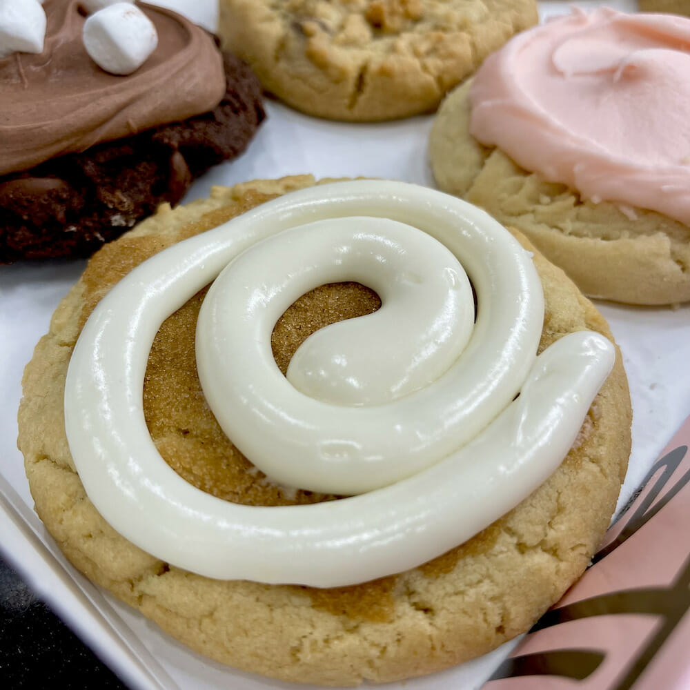 A close up of a Crumbl Cookie with cinnamon and sugar and a spiral of white icing on top.
