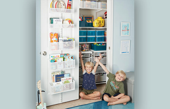 Two kids sitting on the floor in front of an organized closet.