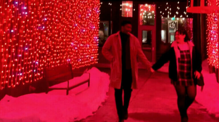 A couple holding hands under the red lights installation at Easton.