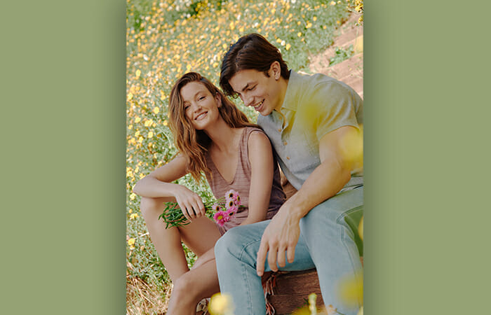 A man and a woman sitting outside in a field of flowers wearing UpWest clothing.