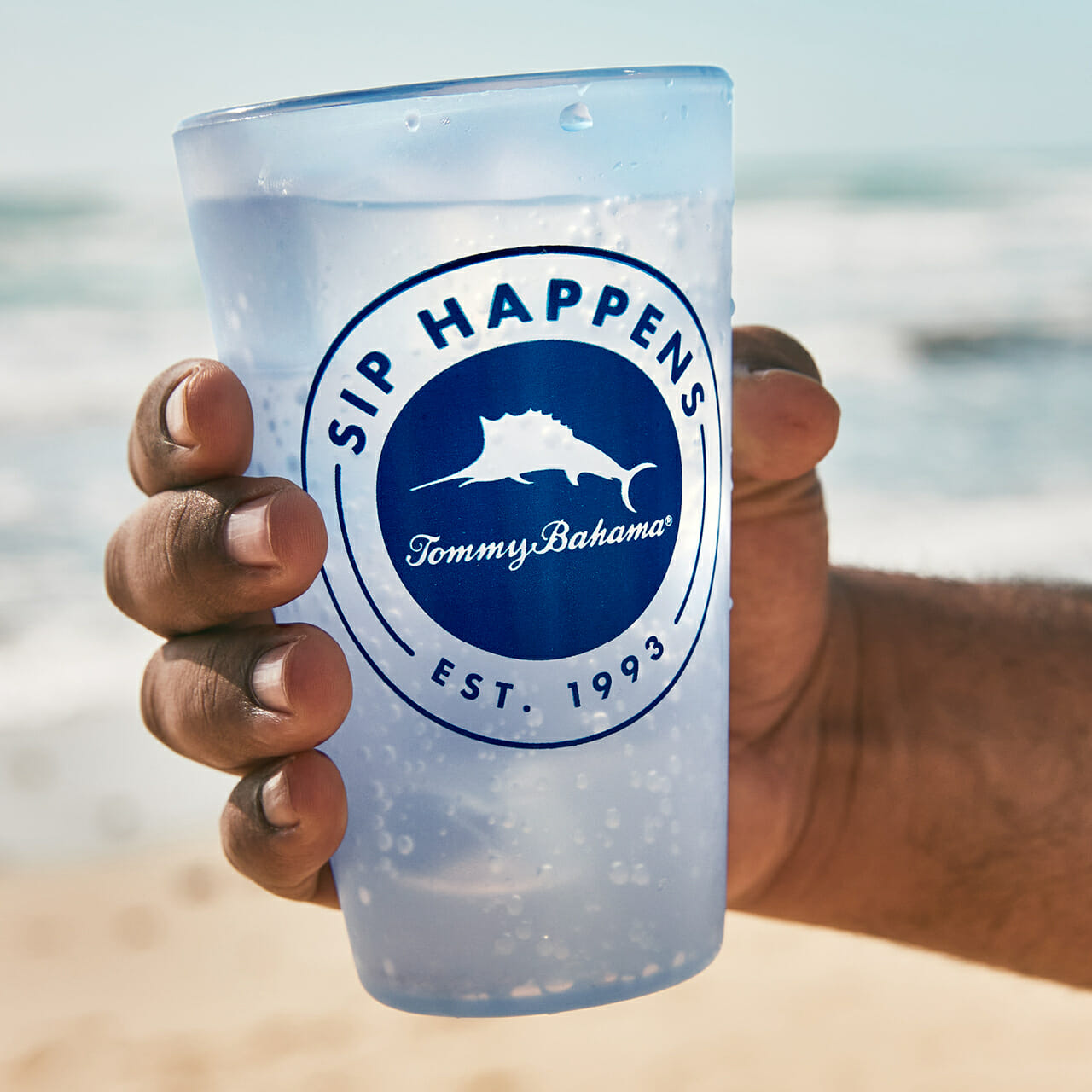 A hand holding a reusable Tommy Bahama cup.