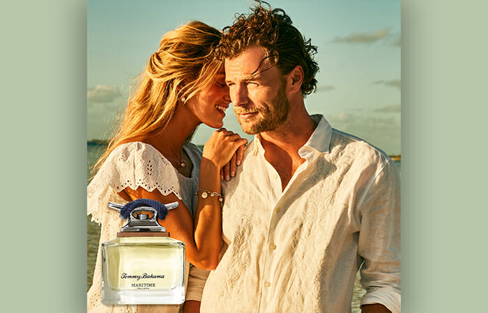 A man and a woman standing on a beach with a bottle of men's cologne in the frame.