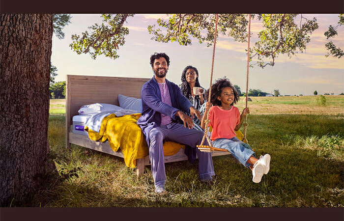 A family sitting on a Purple brand bed.