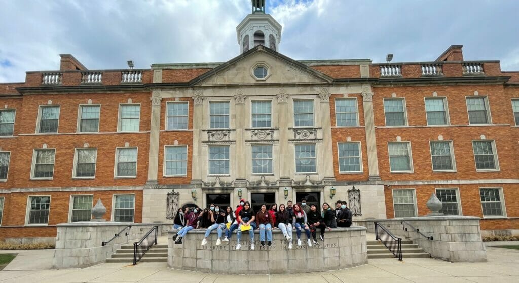 A group of students sitting in front of their school building.