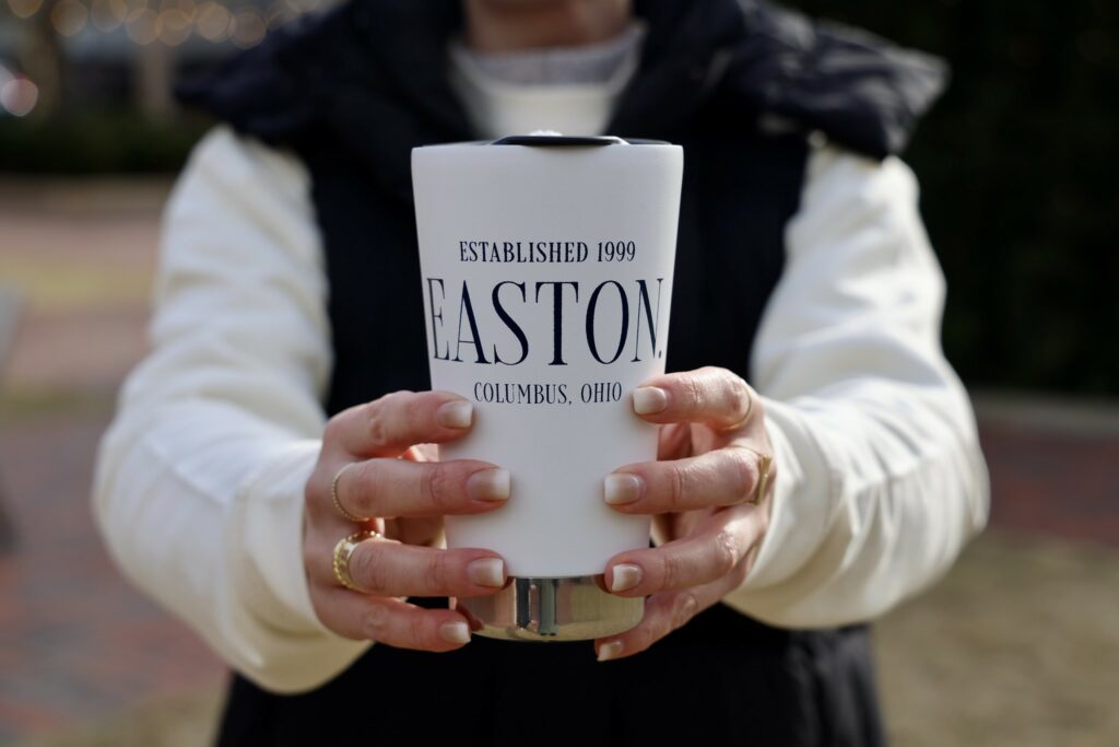A woman holding up an Easton branded travel mug.