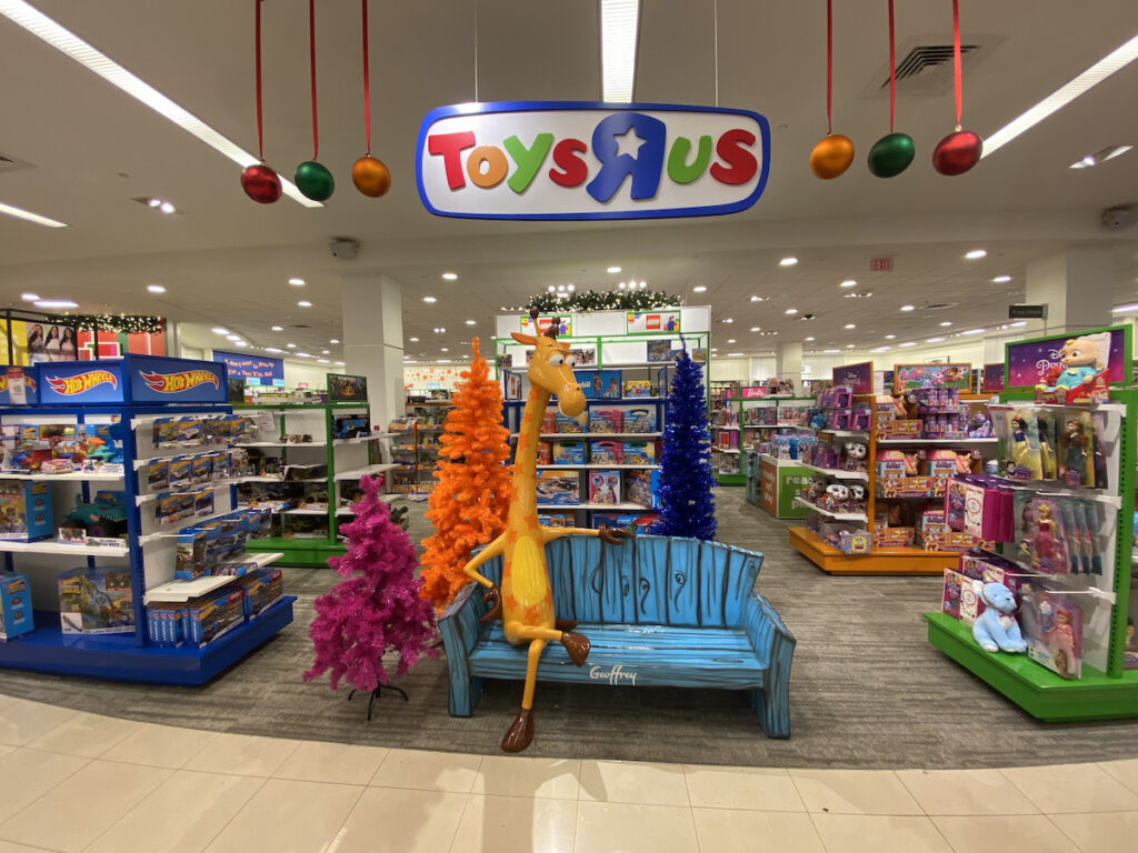 Geoffrey Giraffe sitting on a bench in Macy's Toys "R" Us section