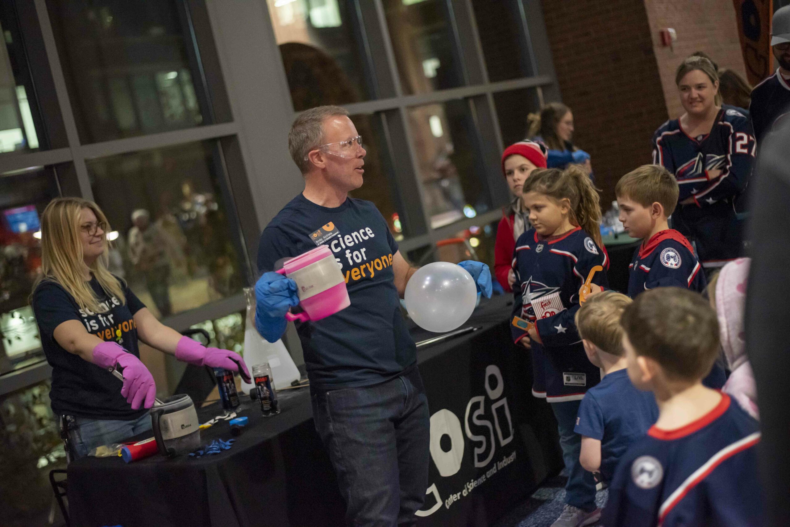 COSI employees doing a science demonstration at a Columbus Blue Jackets game with children and adults watching.