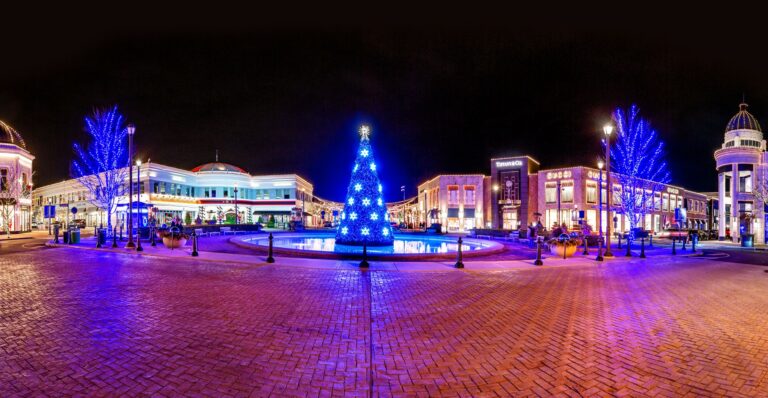 A panoramic view of the Central Park Fountain with holiday decorations at night and surrounding stores at Easton Town Center.