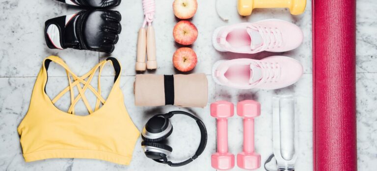 workout gear inclusive of a sports bra, jump rope, a towel, gym shoes, weights, headphones, a water bottle, and apples.