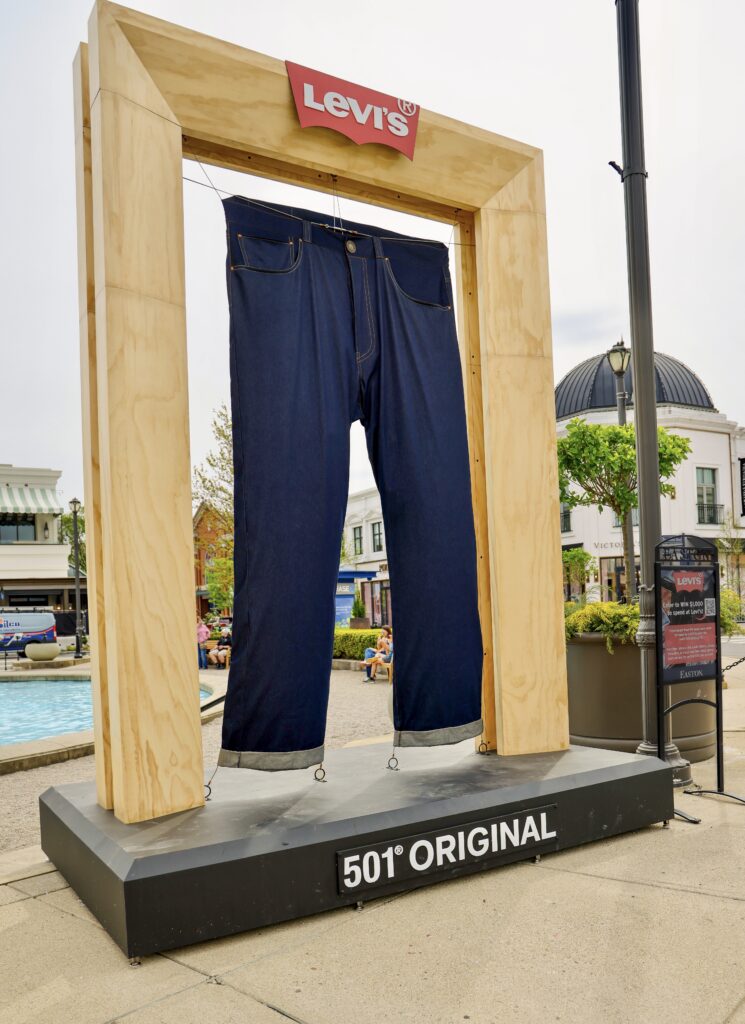 A large oversized pair of Levi's jeans displayed in a large wooden frame and a steel base.