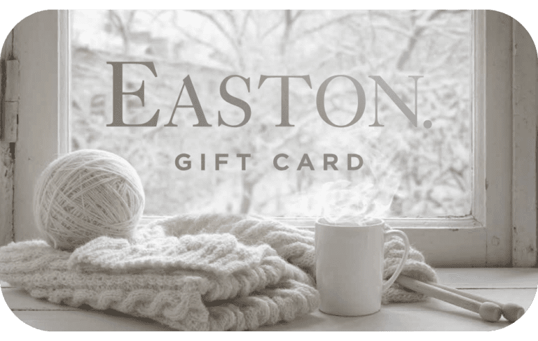 An Easton gift card designed with a snowy window scene background and a wool blanket and a ball of yarn next to a coffee mug.