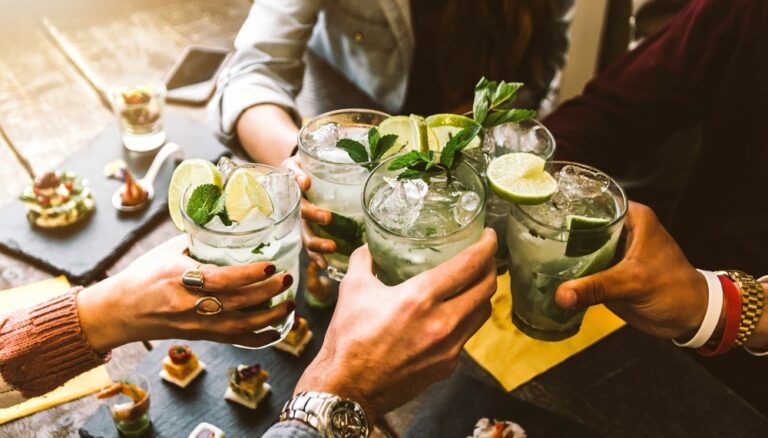 A group of friends cheers-ing with drinks over a table of food.