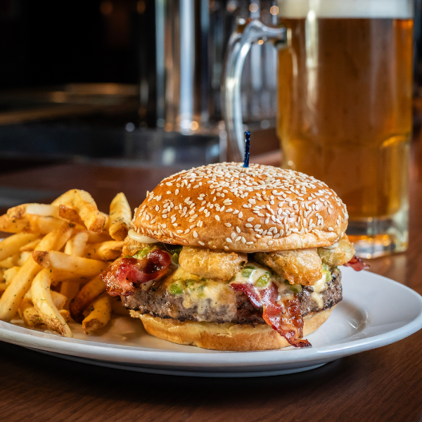 A burger and fries on a plate with a glass of beer in the background from Rusty Bucket.