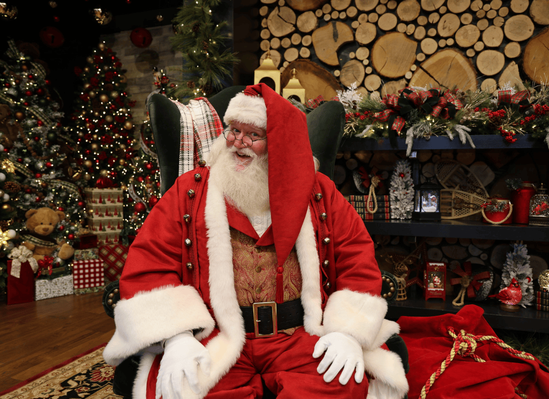 Santa Claus sitting on a chair in front of a holiday decor background.