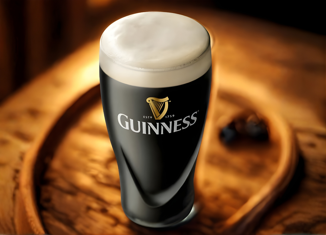 A pint glass filled to the brim labeled with the Guinness logo presented on a rustic wood table.