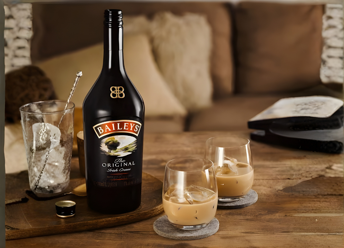 Cozy living room setting with a ice-filled glass, a bottle of Baileys Original Irish cream, and two small glasses filled with Baileys.