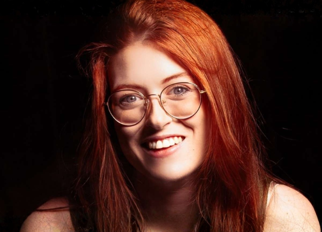 Women with long red hair wearing round glasses smiling towards the camera