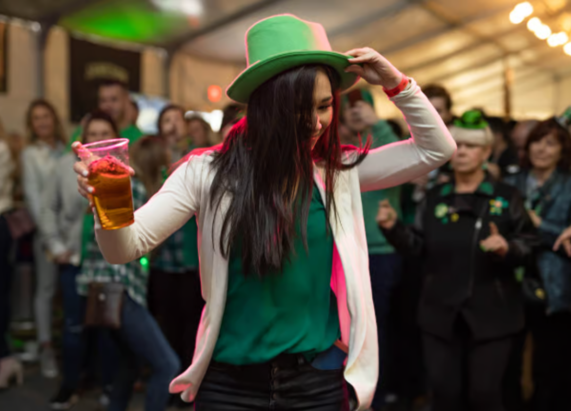 Woman wearing green holding a drink and dancing with a crowd of people in the background