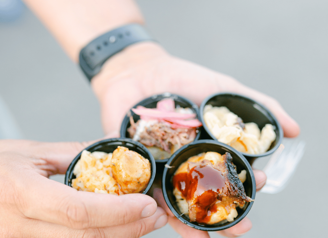 A close up of two hands holding small sample containers of mac and cheese.