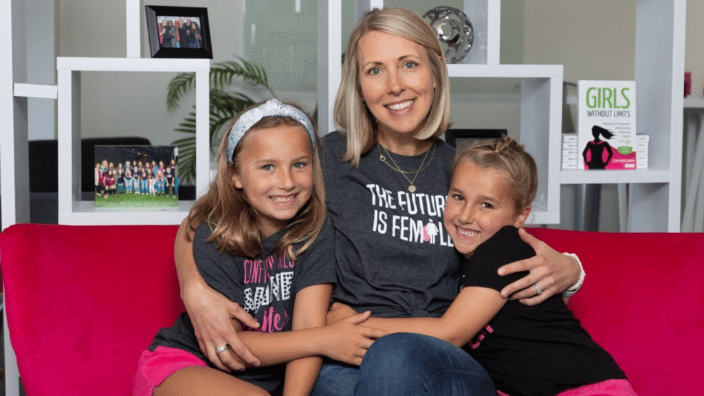 A mother and her two daughters sitting on a couch smiling for the camera.