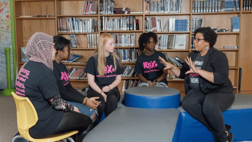A group of girls and a ROX leader having a discussion in a library.